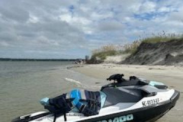 Personal watercraft on sandy beach with dune grass, under partly cloudy sky.