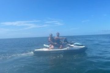 Two people riding a jet ski on a calm blue ocean under a clear sky.