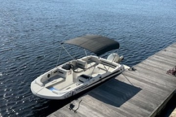 White motorboat with canopy docked beside wooden pier on a sunny day.