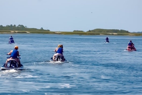 Group of people riding jet skis on a wide blue river with green shores.