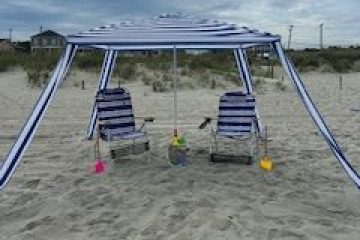 Beach setup with striped canopy, two chairs, toys, and cloudy sky.