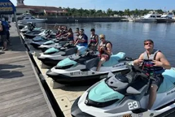 Group of people on jet skis lined up on a dock near a body of water.