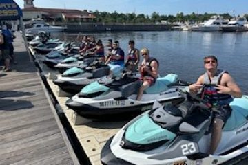 Group of people on jet skis lined up at a dock on a sunny day.