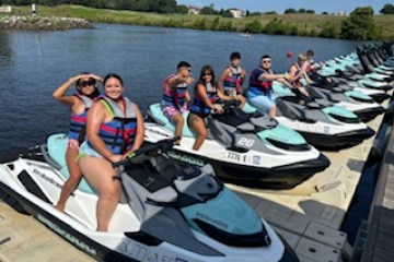 Group of people on jet skis at a dock wearing life jackets on a sunny day.
