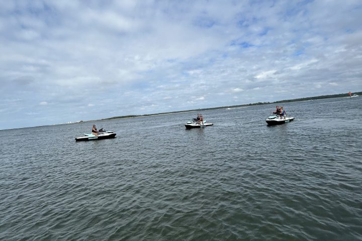 Three jet skis on a calm sea under a partly cloudy sky.