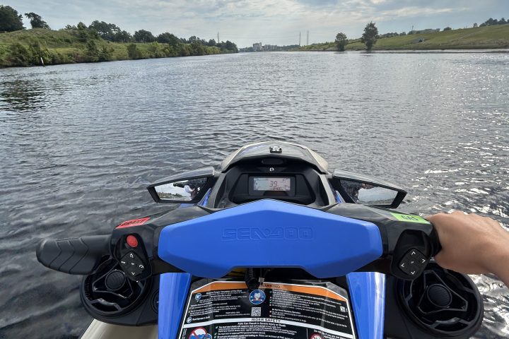 View from a jet ski handlebar on a calm river under a partly cloudy sky.