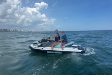 Two people riding a jet ski on a calm ocean under a partly cloudy sky.