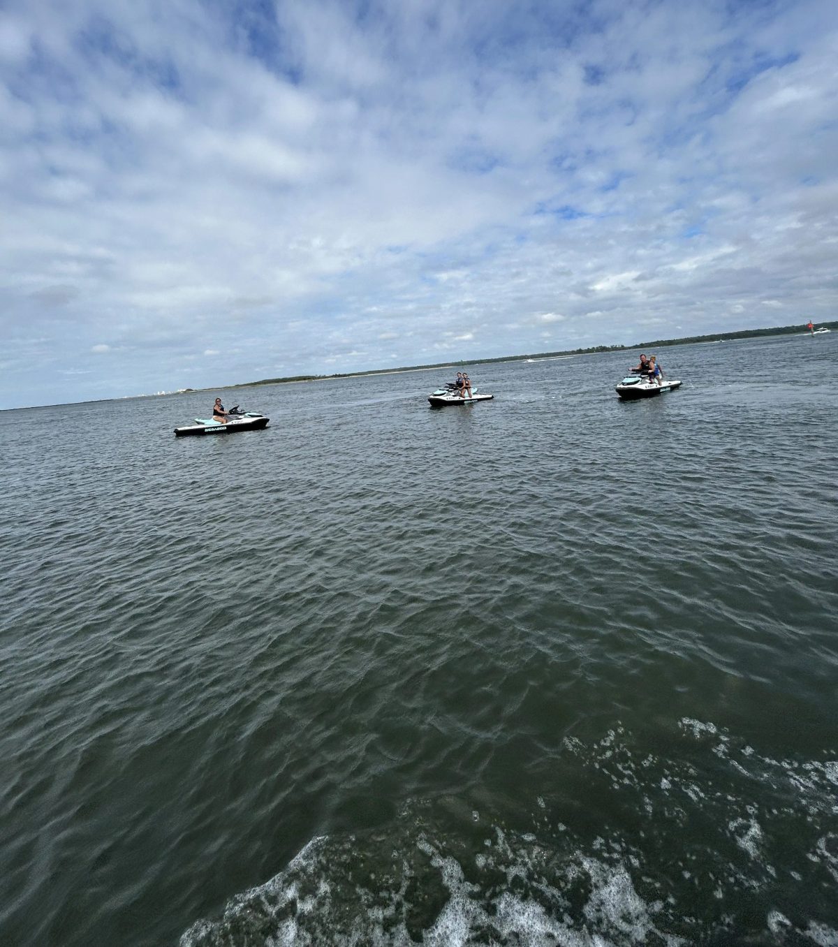 Three jet skis on open water under a cloudy sky.